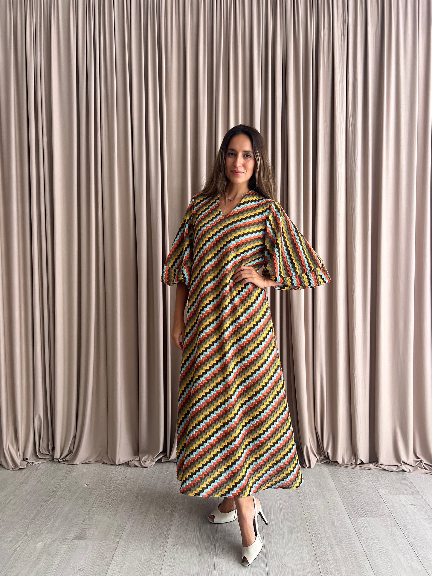 Woman wearing a colorful striped dress standing in front of beige curtains.
