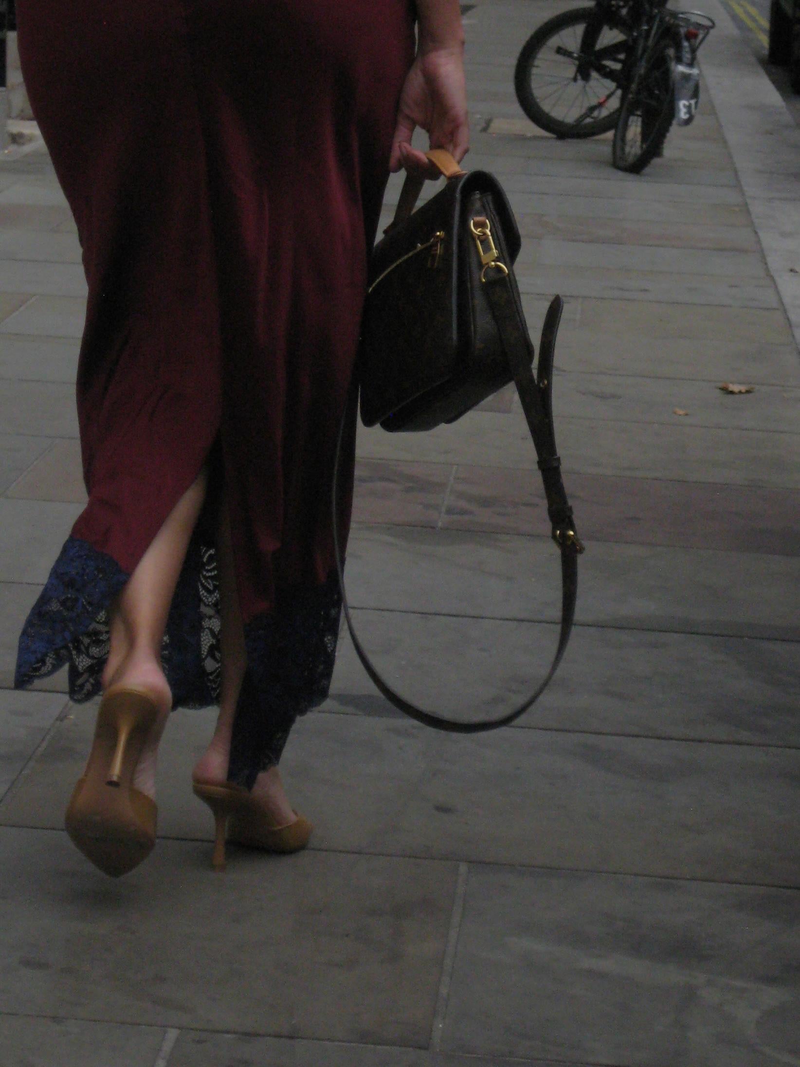 Person walking on a sidewalk with a black handbag